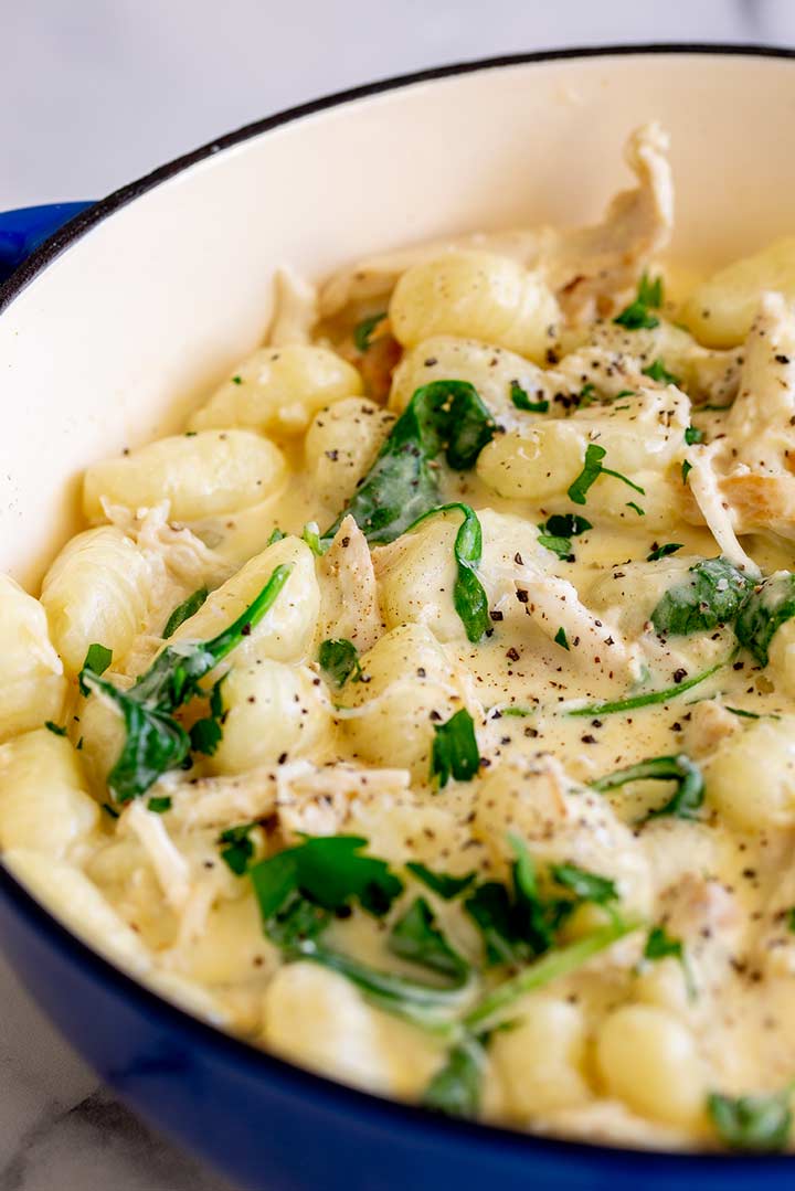 a blue skillet filled with chicken gnocchi and wilted spinach 