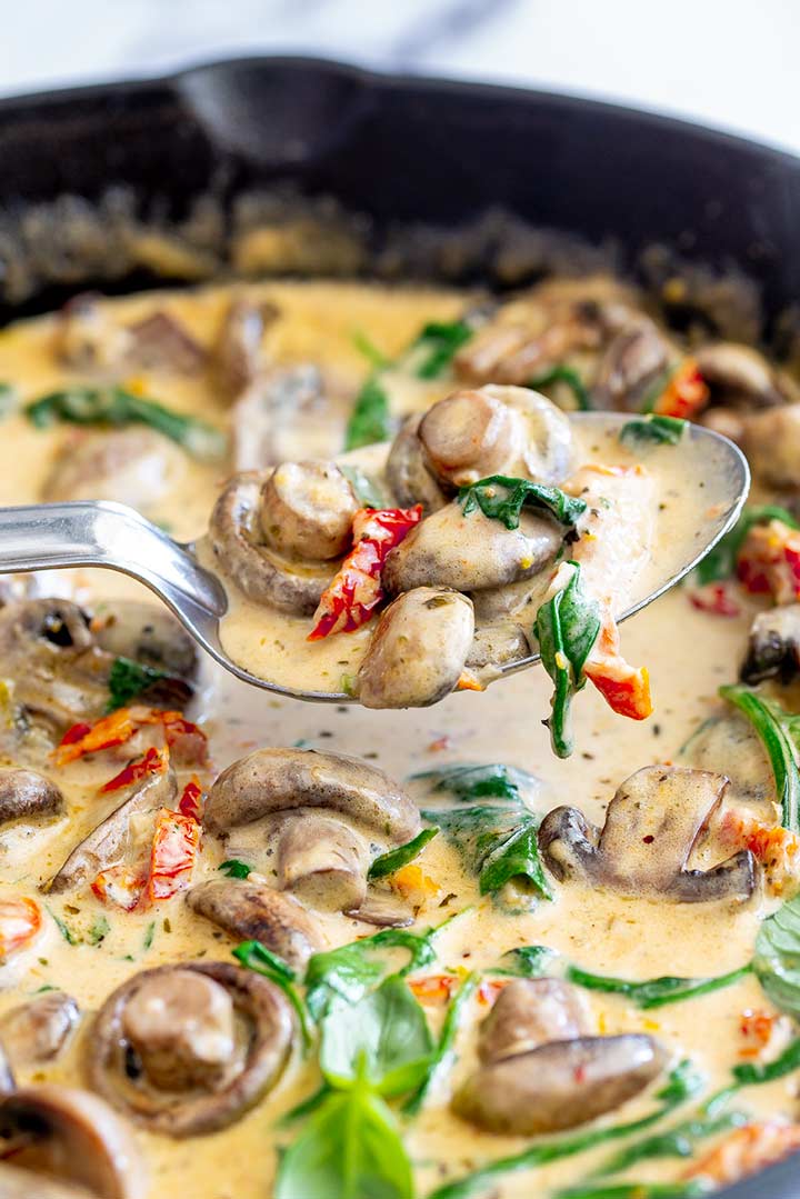 a spoon scooping up tuscan mushrooms from a skillet