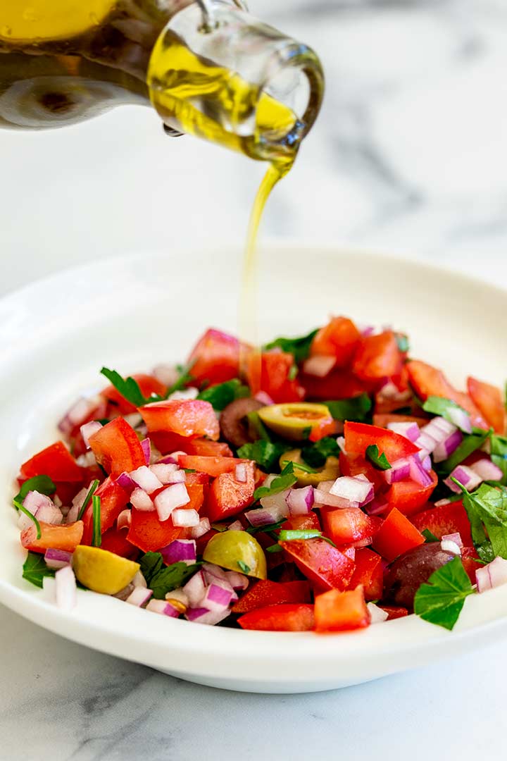 extra virgin olive oil being poured over a tomato onion salad