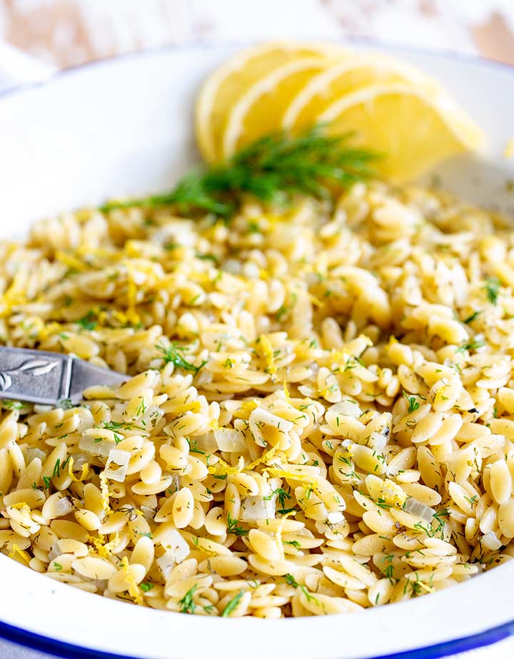 a silver spoon dipped into a bowl of cooked orzo pasta