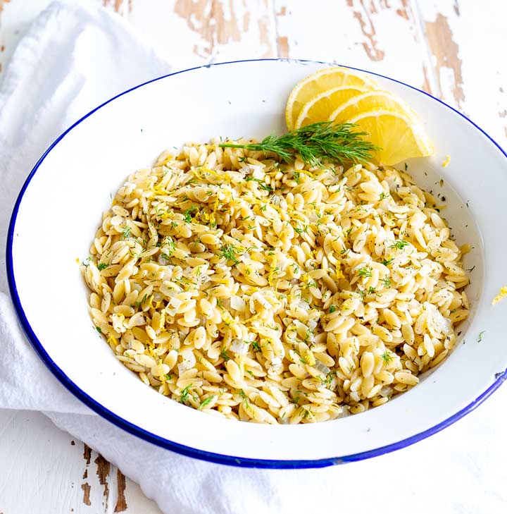 greek orzo in a white bowl with a blue rim on a whitewashed wood table