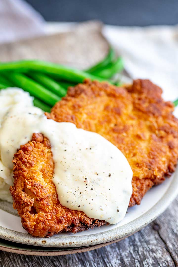 close up on a crispy chicken breast coated in white gravy