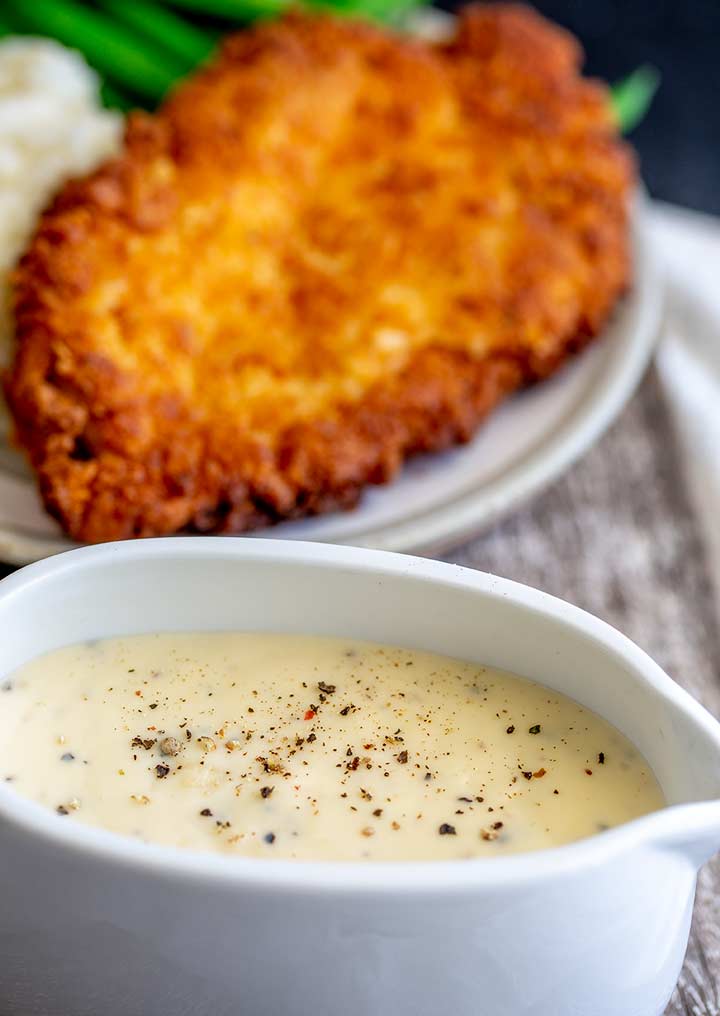 a gravy boat of white gravy with chicken fried chicken in the background