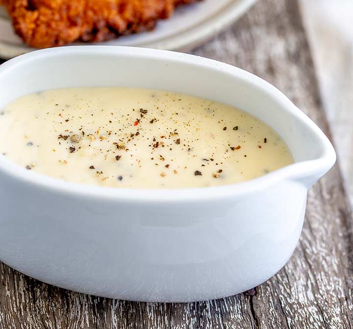 close up on a gravy boat with white gravy in it garnished with pepper