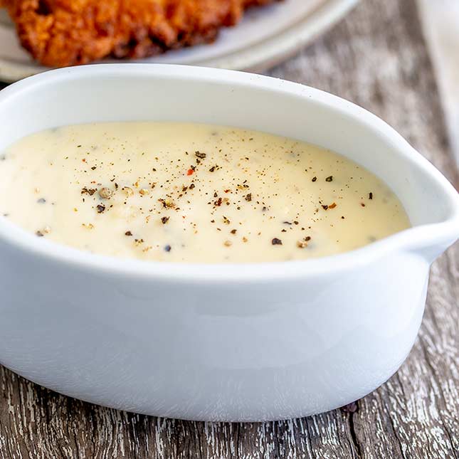 close up on the white gravy in a gravy boat on a wooden board