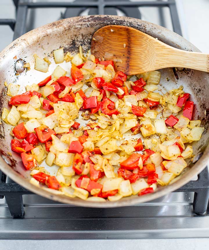 onions and red bell peppers being cooked in a skillet