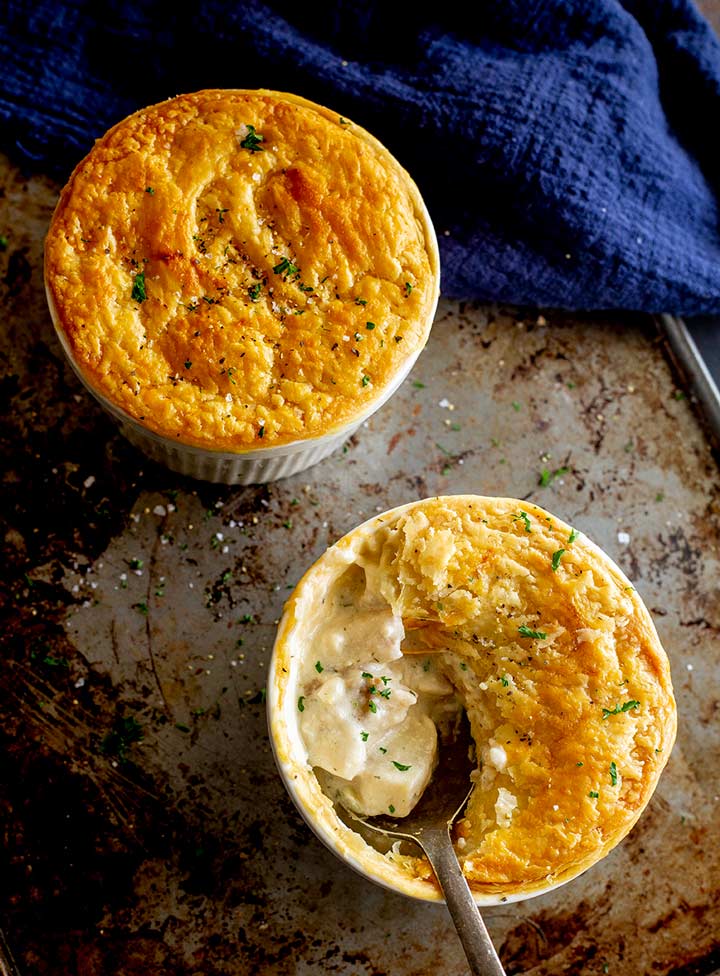 two fish pot pies, one with a spoon in the creamy filling on an old baking tray with a blue tea towel