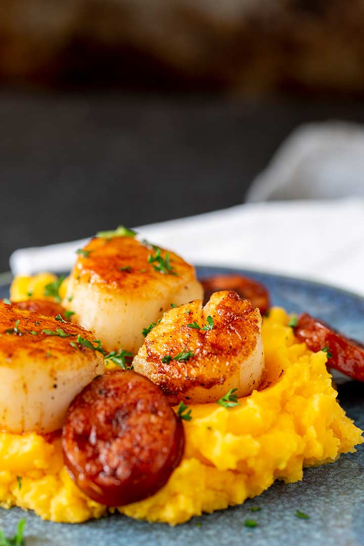 close up on a pan fried scallop on top of sweet potato mash