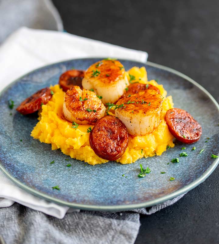a blue plate of sweet potato with scallops and chorizo on top