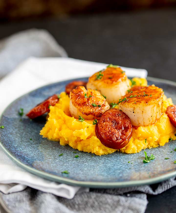 head on view of a blue plate with sweet potato mash, scallops and chorizo garnished with parsley
