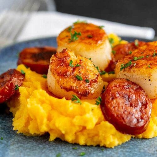 close up square picture of pan fried scallops and chorizo on a pile of sweet potato mash.