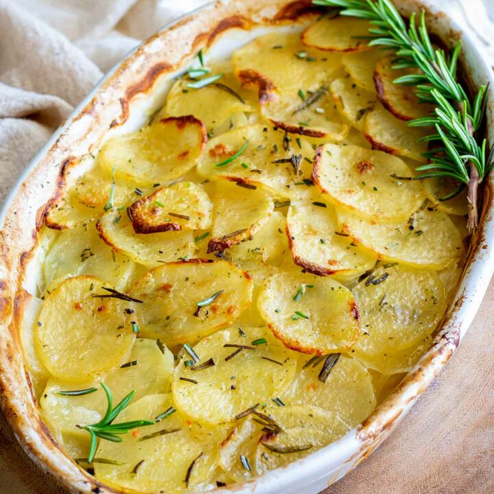 overhead shot of an oval dish of scalloped potatoes garnish with rosemary