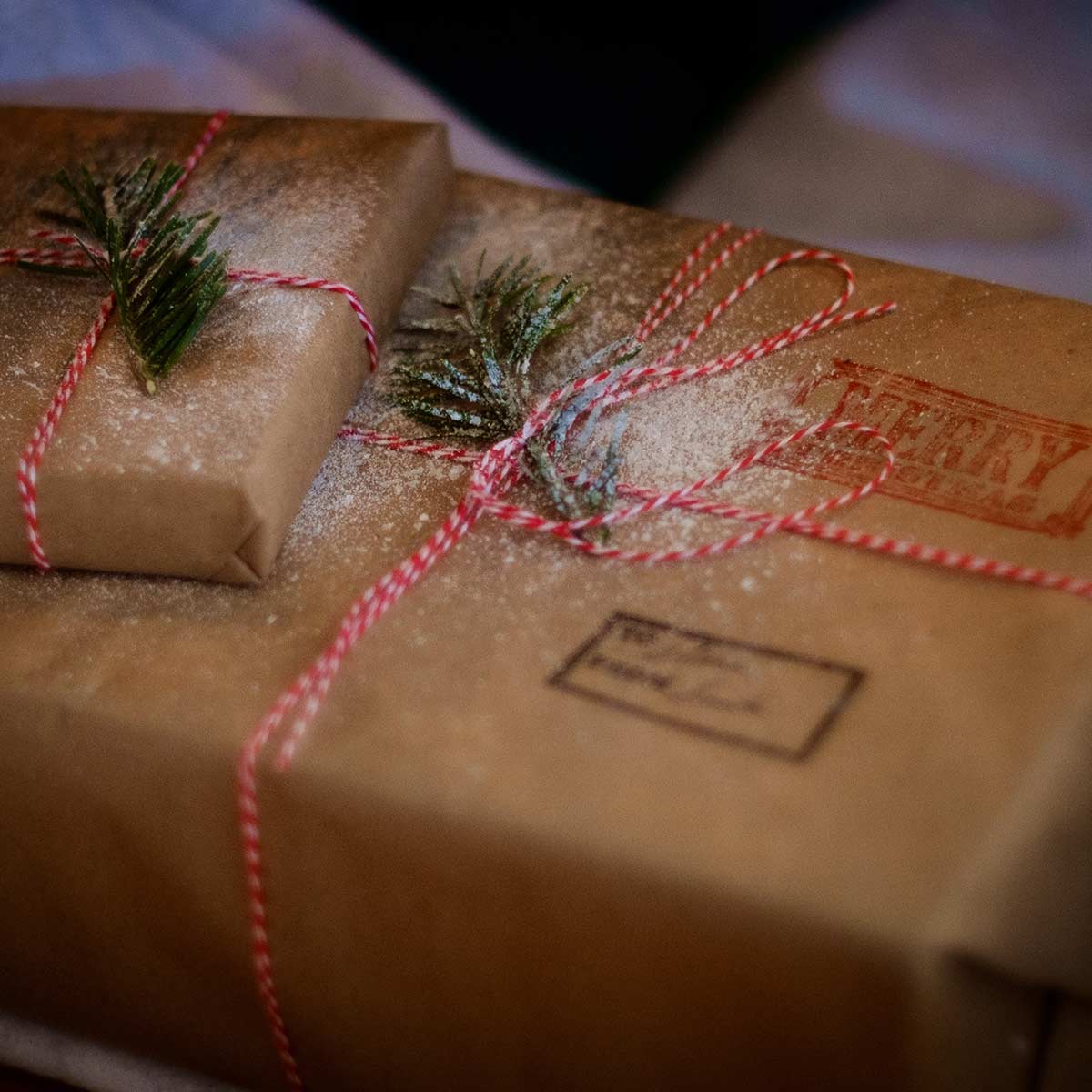 two presents wrapped in brown paper with pine needles and red ribbon