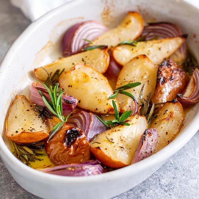 square picture of baked pears and onions in a white oval dish