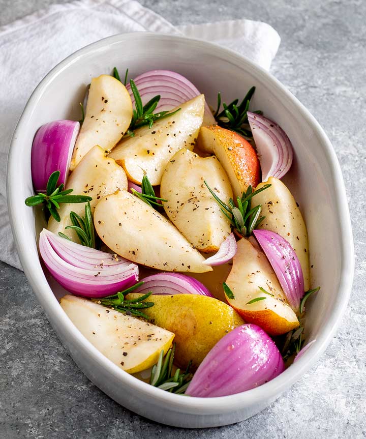 a casserole dish filled with raw pears, onions and rosemary
