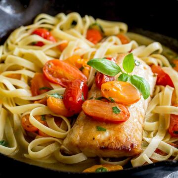 square picture showing a cooked cod fillet on a bed of tomato pasta