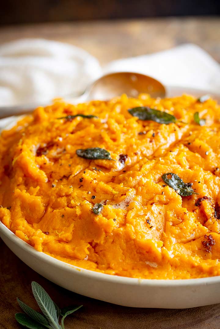 a cream bowl filed with sweet potato mash with crispy sage leaves on a wooden board