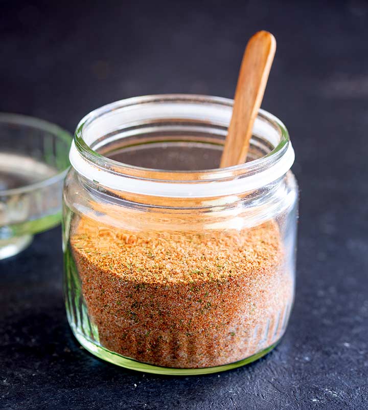 a glass jar of peri peri seasoning on a black table with a wooden spoon sticking out of it