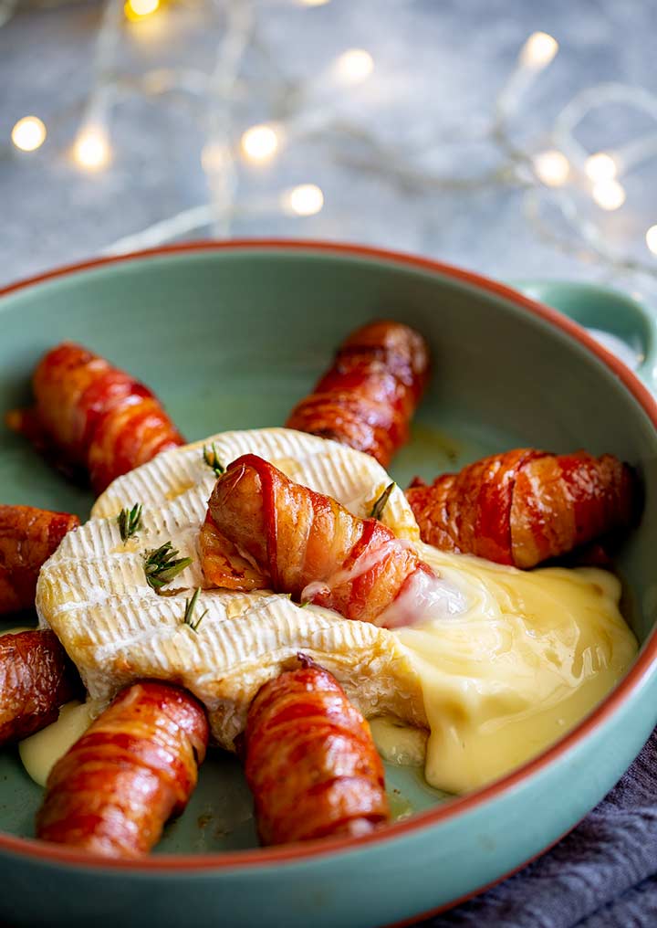 a bacon wrapped sausage sitting in a pool of melted hot brie