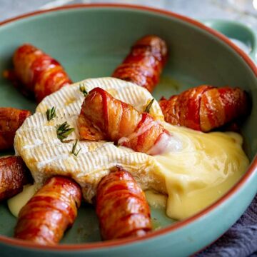 close up on a bacon wrapped sausage laying in molten brie