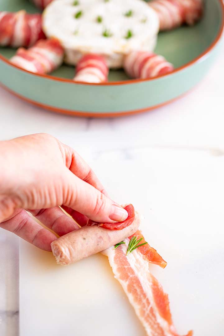 a sausage being rolled up in bacon with a green dish in the background