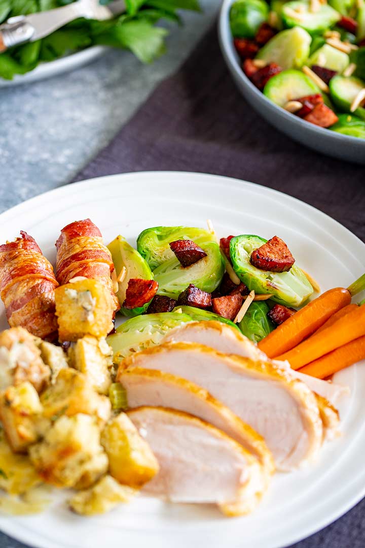 a white plate of turkey, stuffing, sausages in bacon, carrots and brussel sprouts