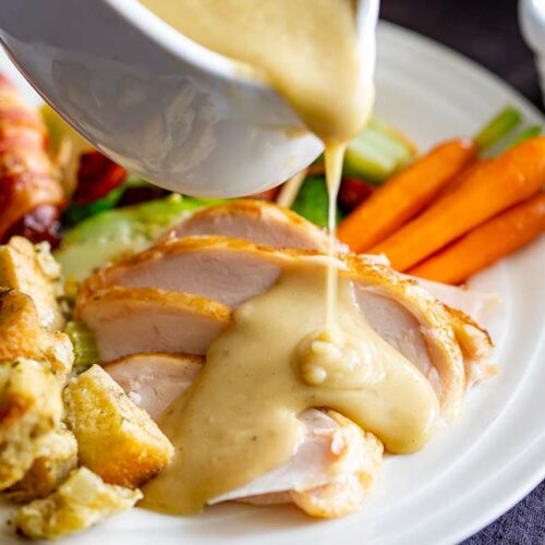 a pale gravy being poured over slices of turkey