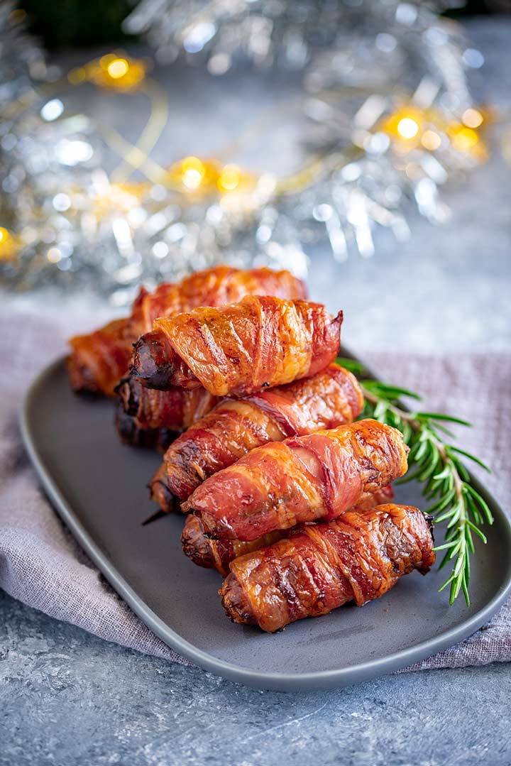 a grey plate of bacon wrapped sausages with tinsel and fairy lights behind