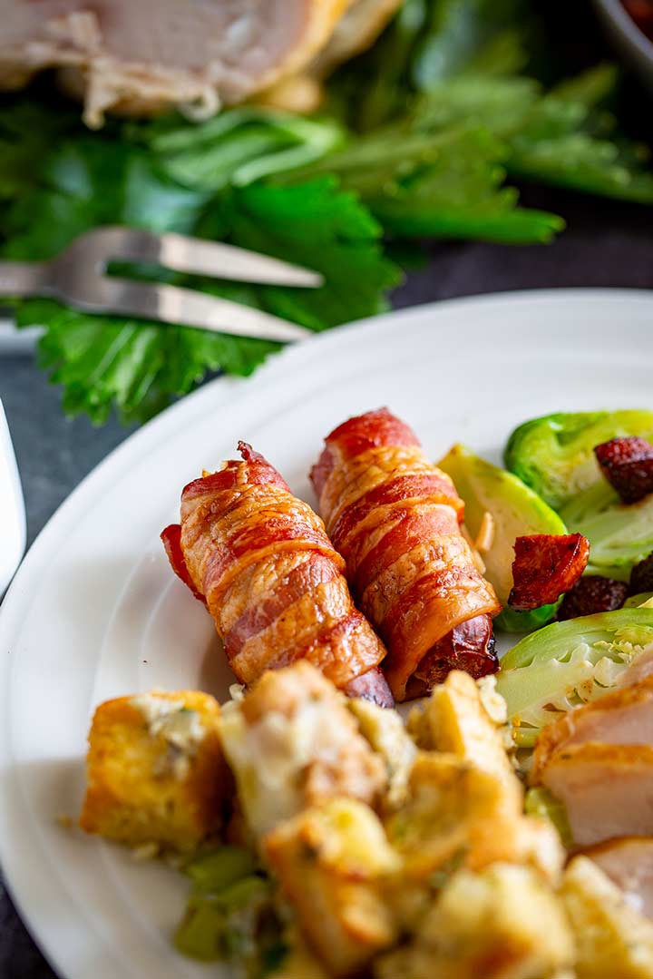 two sausages wrapped in bacon on a white plate with Christmas dinner