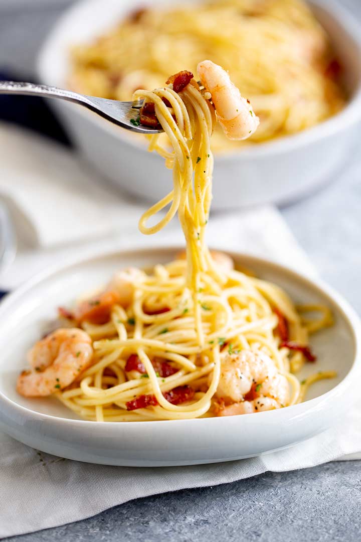 a fork lifting up a shrimp and some spaghetti from a white plate