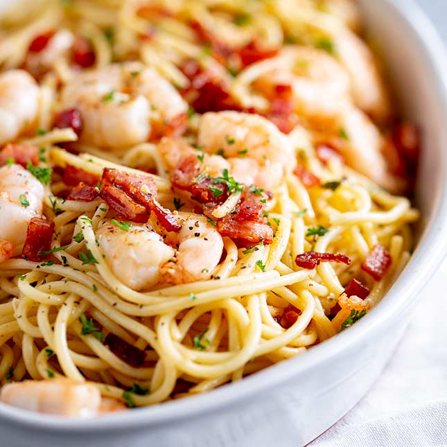 Close up on spaghetti in a white oval dish with bacon and shrimp