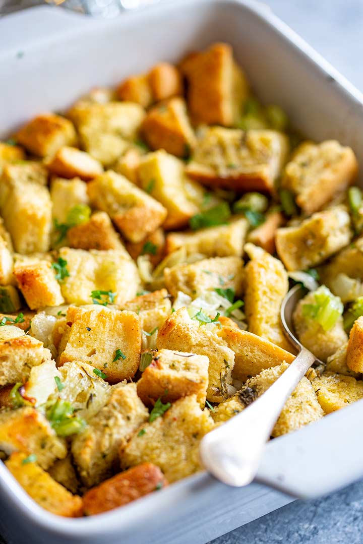 a spoon sticking into a white dish of cubed bread stuffing
