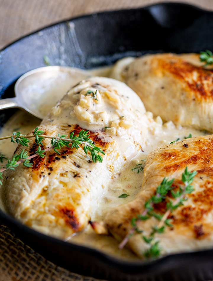 a spoon in a white wine sauce with chicken breasts and thyme