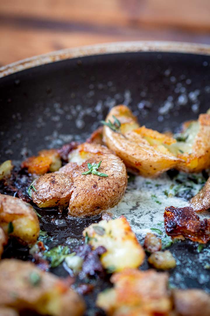 a smashed baby potatoes in a skillet with butter and herbs