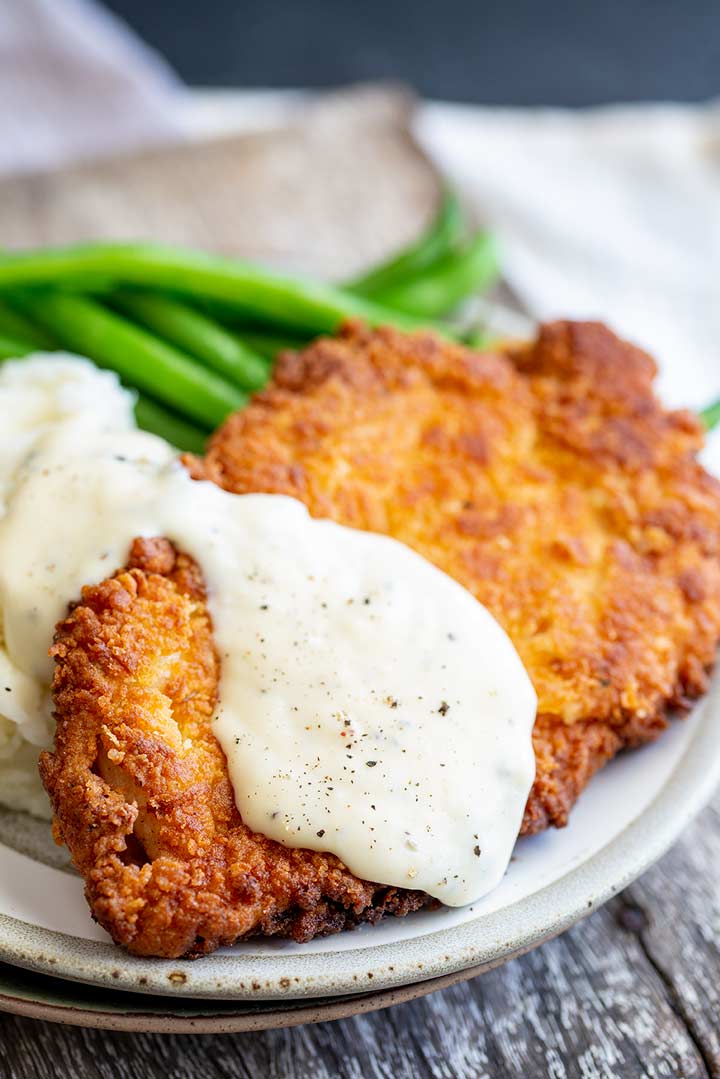 a chicken fried chicken fillet with white gravy and green beans