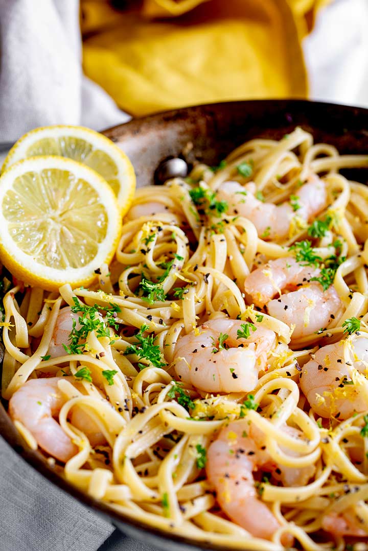 a metal pan of shrimp and pasta with lemon slices on the side