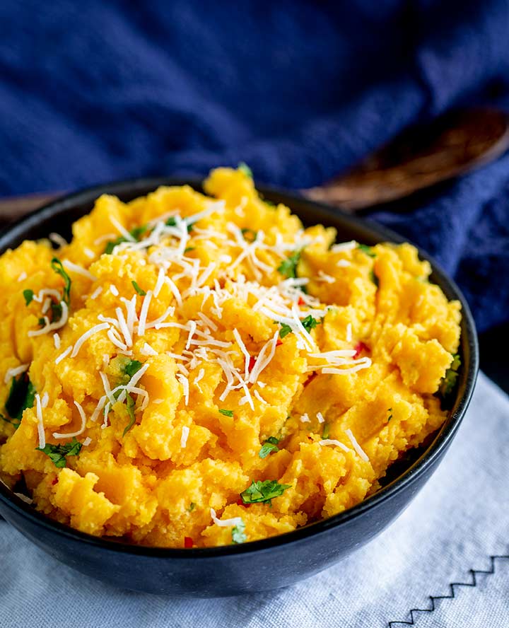a clack bowl on a white mat with sweet potato mash with shredded coconut and cilanto on top