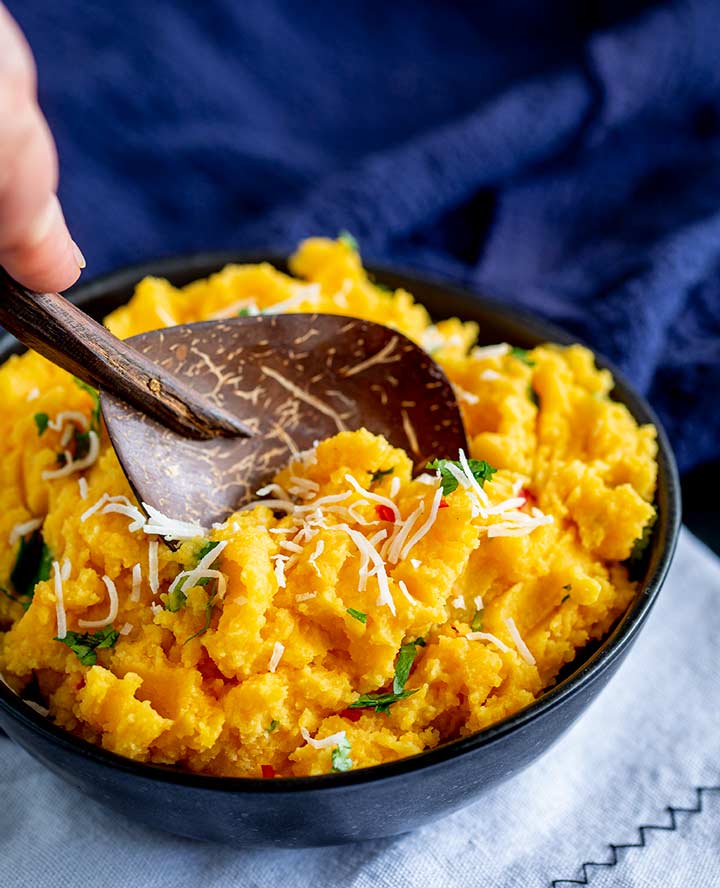 a wooden spoon in a black bowl of Thai sweet potato mash with a blue napkin