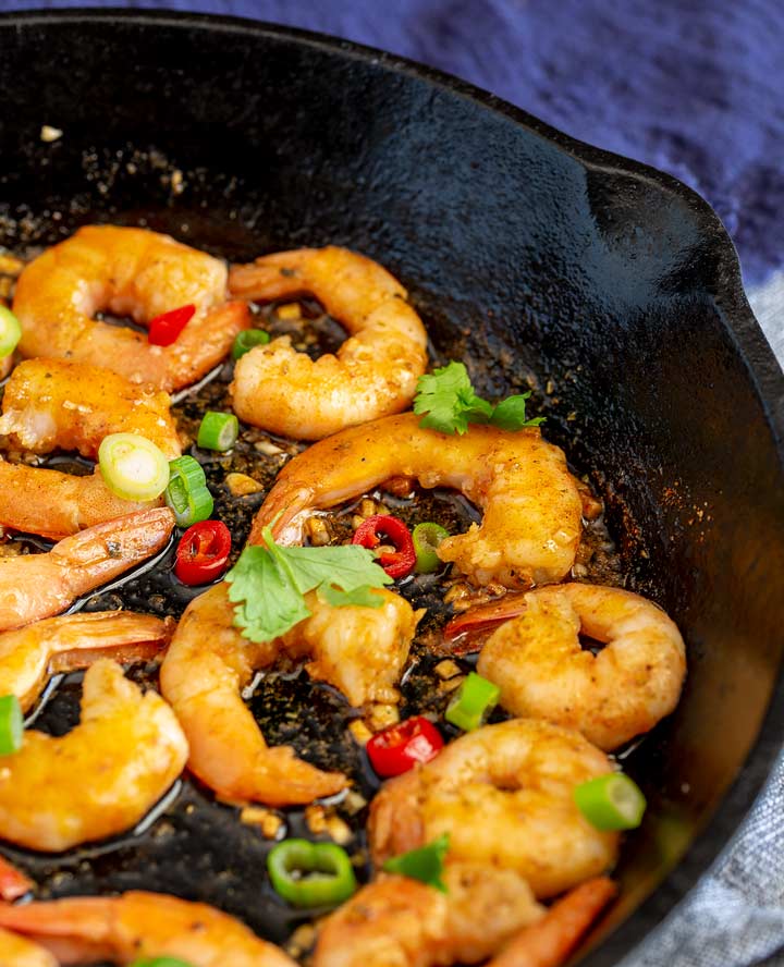 cajun shrimp in a black cast iron skillet garnished with green onion and chili