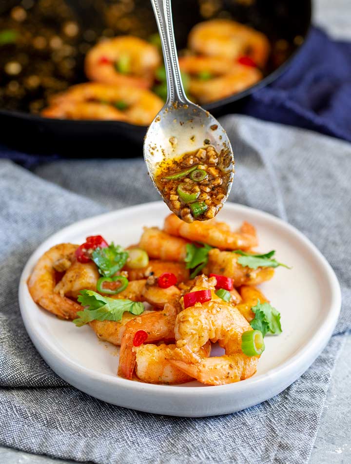 a spoon drizzling garlic cajun butter over cooked shrimp on a white plate