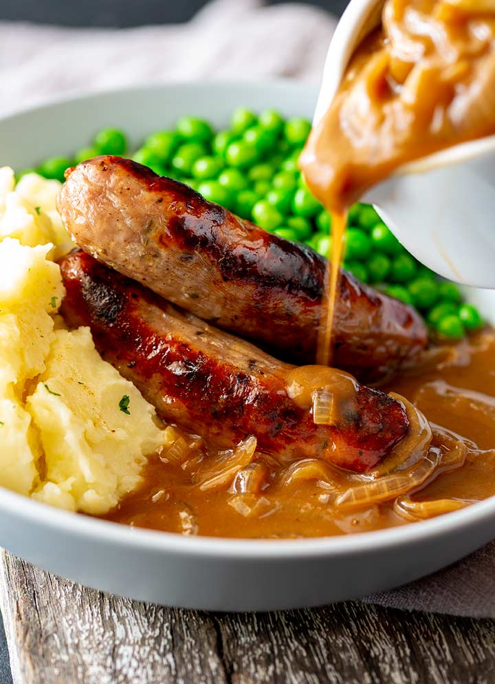 gravy being poured over sausages and mashed potato