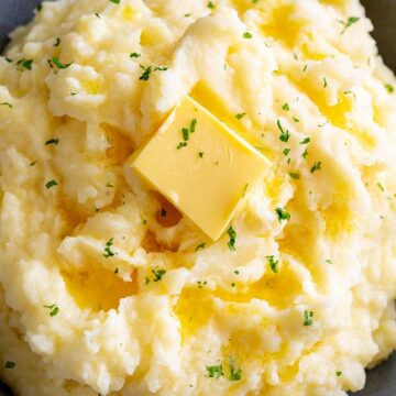overhead of butter square melting over mashed potatoes with parsley garnish