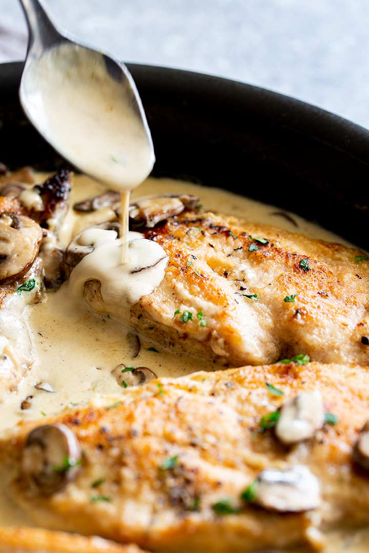 a creamy sauce being spooned over chicken breasts