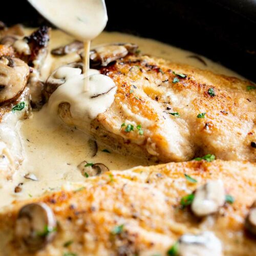 close up of creamy mushroom sauce drizzling over cooked chicken breasts