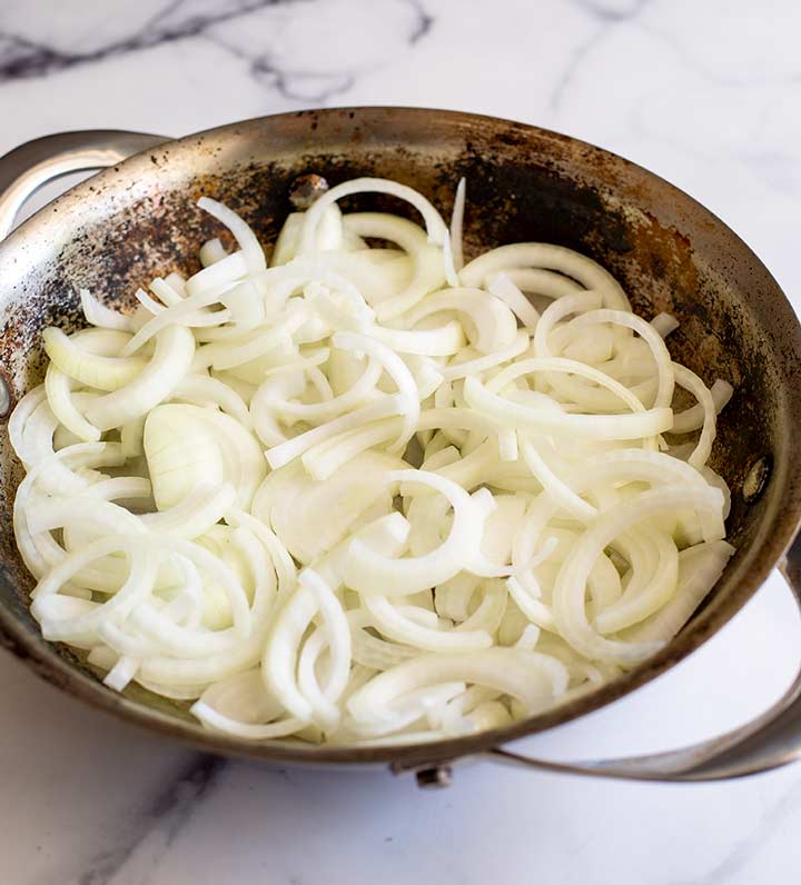 raw onions in a metal pan on a marble counter