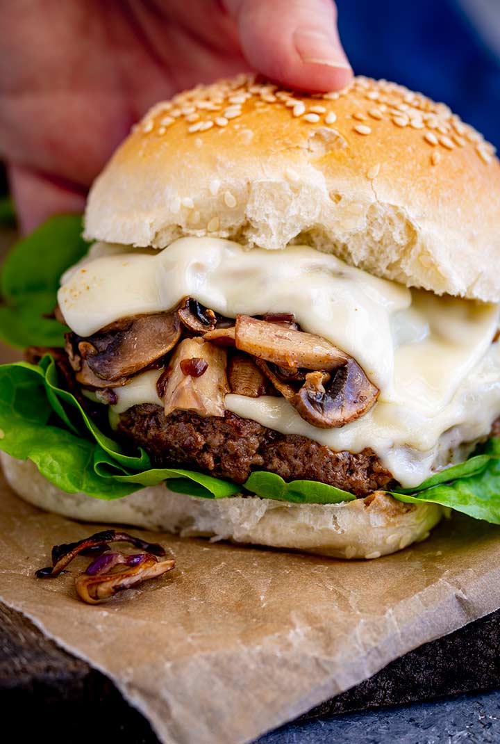a hand picking up a burger with mushrooms and cheese
