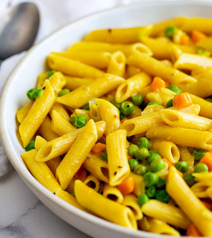 a white bowl of yellow pasta with peas and carrots