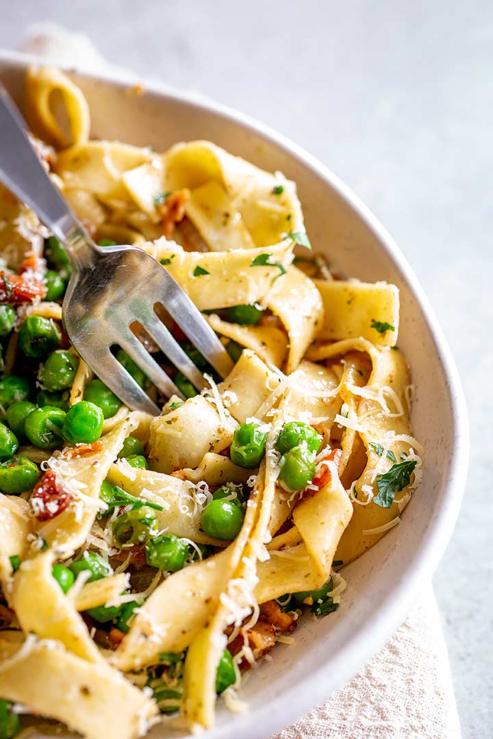 a fork digging into a bowl of pappardelle and peas