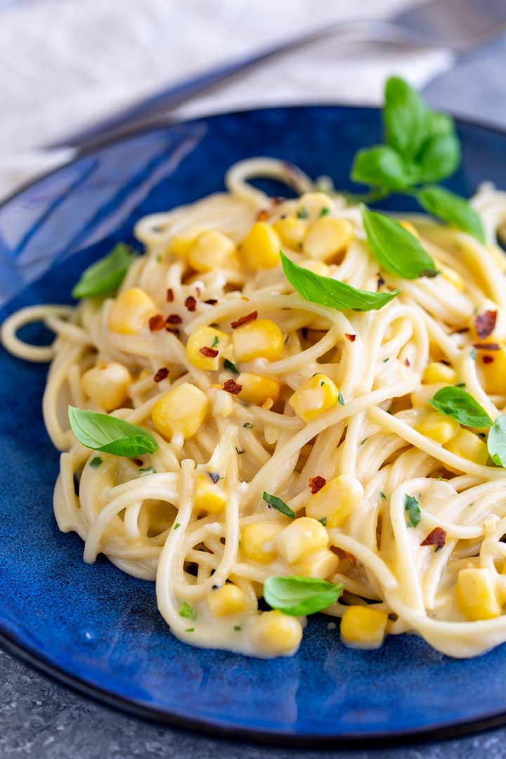 a blue plate of creamy spaghetti with corn and basil