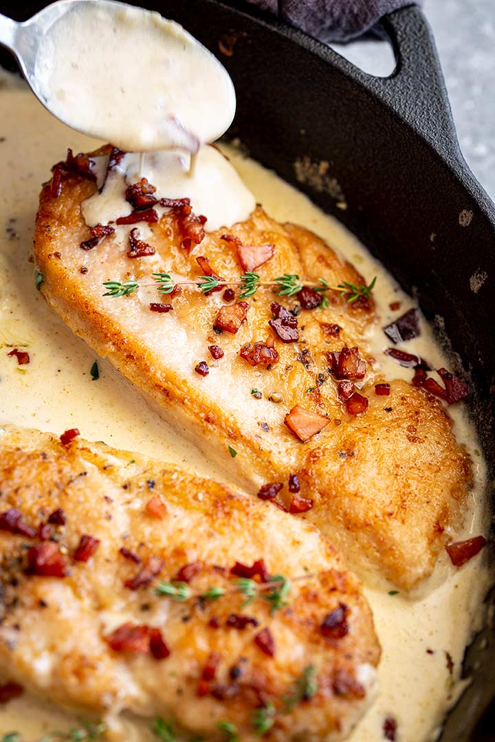 a spoon drizzling creamy sauce over a chicken breast